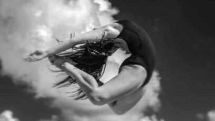 Black and white editorial photo of Mia Bella McGarity leaping mid-air against clouds